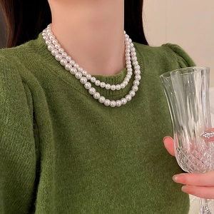 Close-up of double layer white pearl necklace on model wearing a green sweater