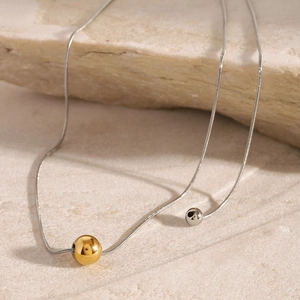 Detail of minimalist gold and silver bead pendants on sleek snake chains on stone surface