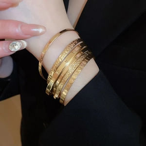 Detail of stacked gold bangles with LOVE engraving and textured patterns on black sleeve