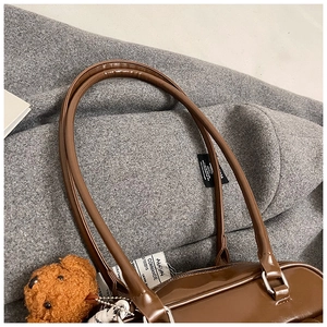 Detail of vintage brown PU leather pillow bag featuring plush bear charm and dual straps