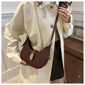 Brown leather crescent bag with gold buckle shown worn by a model in a lifestyle setting