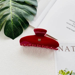 Close-up of a red acetate hair claw clip with a golden B letter logo on white paper