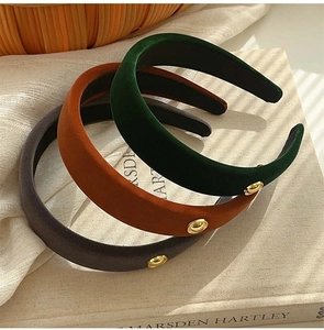 Close-up of velvet sponge headbands in dark green, rusty red, and grey with gold emblems