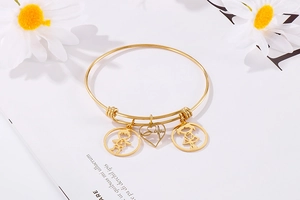 Adjustable gold bracelet with boy, girl, and heart charms on a white book background