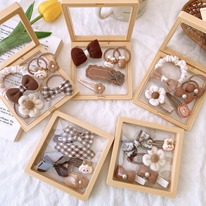 Flat lay of five earth-toned hair accessory gift sets on white fabric with tulips