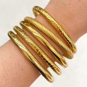 Detailed close-up of five gold-plated bangles with unique textures on model's wrist