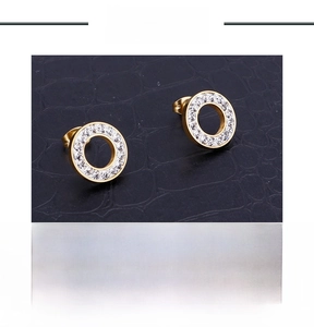 Close-up of golden stainless steel round earrings with crystal pavé on black texture