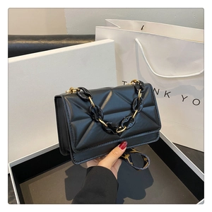 Close-up of black quilted crossbody bag with resin chain and geometric pattern strap