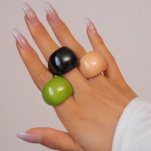 Three colorful geometric resin rings in black, green, and nude on a model's hand