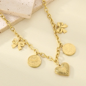 Detail of layered gold heart and coin charms on a minimalist textured fabric background