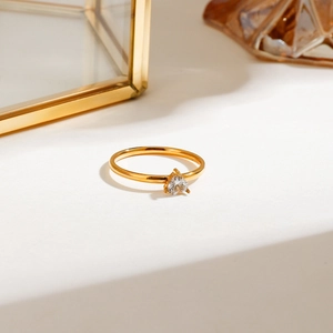 Close-up of golden ring with heart-shaped crystal on a minimalist beige display stand
