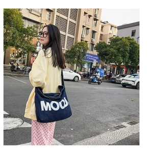 Deep blue denim tote bag with MOOD lettering shown in a stylish urban street setting