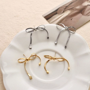Minimalist knotted bow earrings in gold and silver finish on a ceramic tray