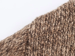 Close-up of thick cable knit fabric showing soft wool texture and mixed brown yarn