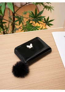 Glossy black zipper wallet with a white butterfly ornament and a soft faux fur pompom detail