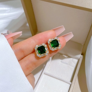 Macro detail of gold-plated square stud earrings with green emerald-cut stones and zircons