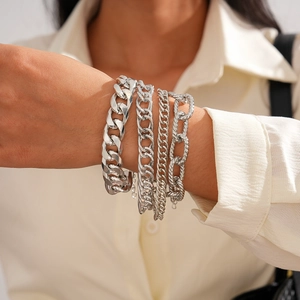 Close-up of four layered silver chain bracelets including Cuban and round link styles