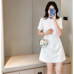 Silver metallic heart-shaped acrylic bag with chain strap held by a model in a white dress
