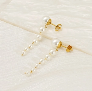 Detail of long gold tassel earrings with gradient white pearls on white textured background