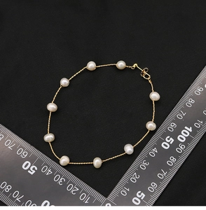 Close-up of pearl bracelet with gold twisted chain on black fabric showing length detail