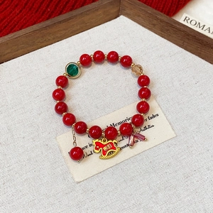 Detail of red beaded lucky bracelet with golden pony charm and crystals on wooden tray