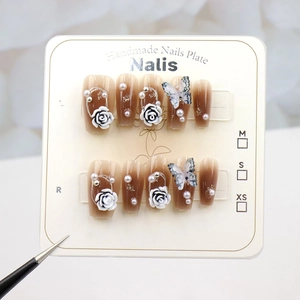 Detail of brown gradient press-on nails with 3D white roses and pearls on a display card