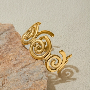 Elegant gold spiral hollow open bangle in stainless steel displayed on a natural stone base