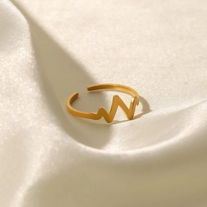 Macro view of gold-plated stainless steel heartbeat ring on a soft beige silk fabric