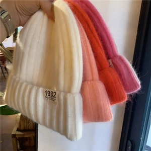 Close-up of soft knitted beanies in white, pink, and orange with 1982 embroidery