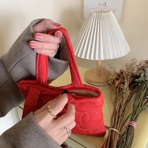 Close-up of a red quilted bunny handbag with floral stitching and a black zipper closure