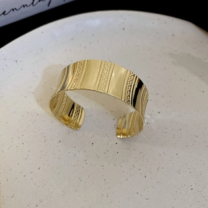 Detailed macro view of wide golden open bangle featuring a wave texture and vertical stripes