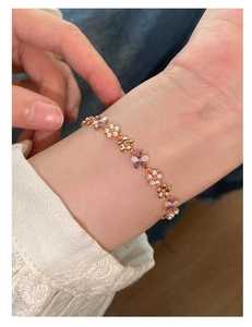 Detailed view of a rose gold flower bracelet with pearls and purple zircons on wrist