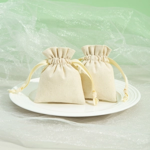 Two beige cotton drawstring jewelry bags displayed on a white plate with green tulle