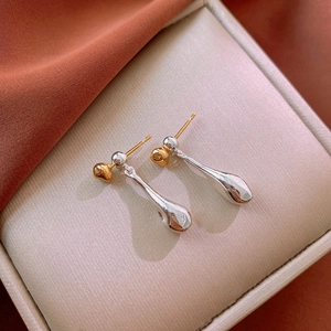 Macro shot of two-tone gold and silver teardrop earrings on a beige textured jewelry cushion