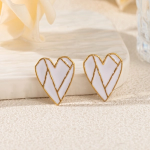 Macro detail of heart-shaped gold earrings with white enamel and geometric gold lines