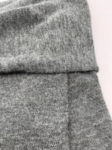 Detail of grey knitted fabric texture showing fine weave and stitching on an off-shoulder sweater