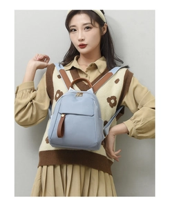 Detailed back view of a mini light blue oxford backpack with brown leather strap accents