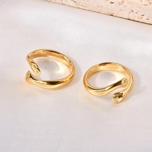 Macro shot of gold-plated embrace hand rings on a white silk and stone surface