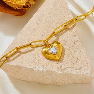 Détail macro d'un pendentif cœur doré avec cristal sur chaîne trombone et tissu en soie