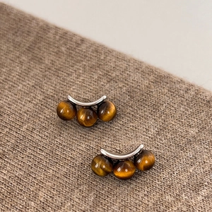 Macro detail of three-bead tiger eye earrings on brown knit fabric with silver metal base