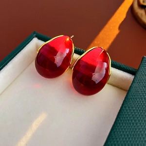 Close-up of red water-drop resin earrings with gold metal accents in a green gift box