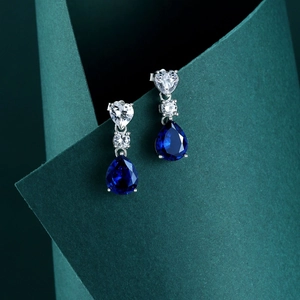 Detailed shot of pear-cut blue gemstone earrings with heart-shaped cubic zirconia accents