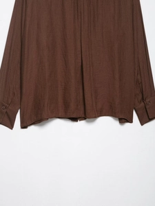 Detailed view of the dark brown textured shirt hem and cuffed long sleeve fabric
