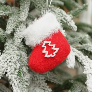 Red plush Christmas stocking ornament with white tree patch hanging on a snowy pine branch