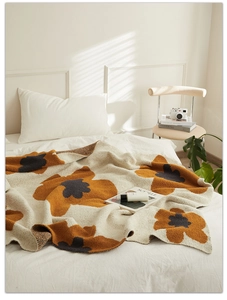 Close-up of cream knit blanket featuring orange and grey floral patterns on a white bed