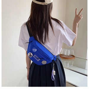 Detail of royal blue crossbody bag featuring astronaut pendant and fashion badges on model