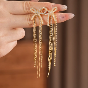 Close-up of gold bow earrings with zircon stones and elegant long fringe tassels