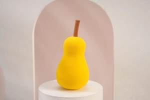 Macro detail of a yellow pear-shaped makeup sponge on a white pedestal with soft shadows