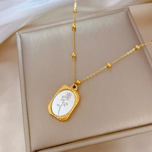 Gold beaded titanium steel necklace with rectangular rose pendant on a beige jewelry box