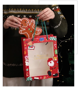 Red Christmas paper gift bag with window and gingerbread man decoration held by model